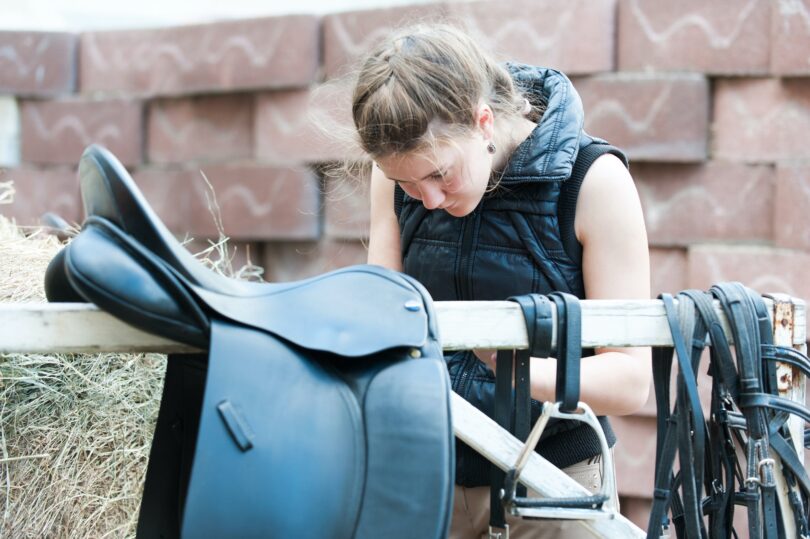 woman putting girth on saddle