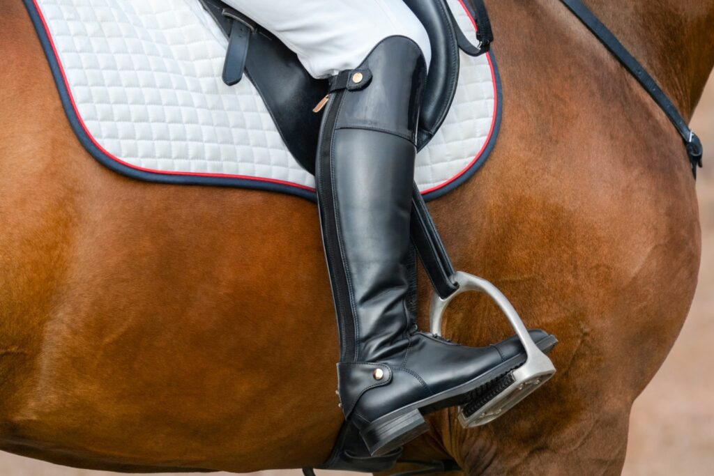 tall black english riding boot against brown horse and white saddle pad