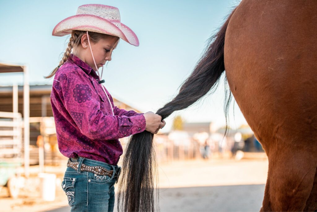 girl in pink braiding a horse's tail