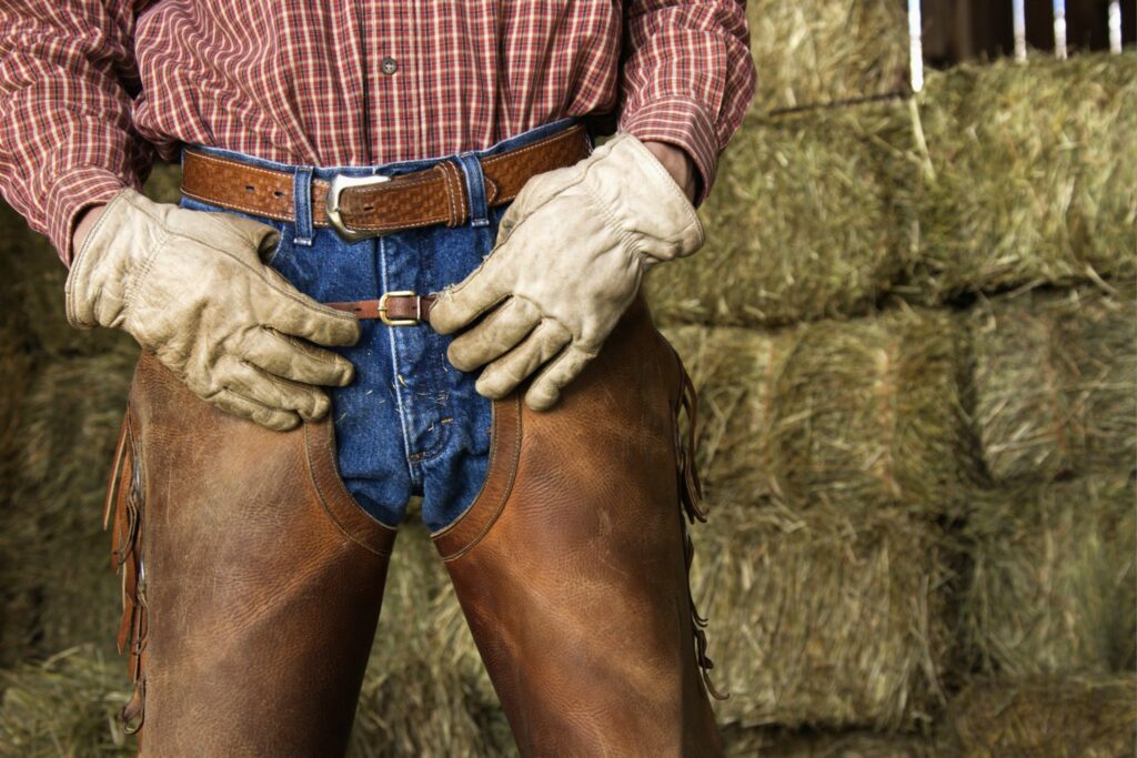 Man wearing leather chaps in front of stacked hay