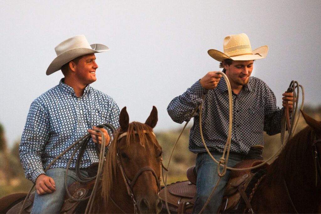 two cowboys riding horses with rope