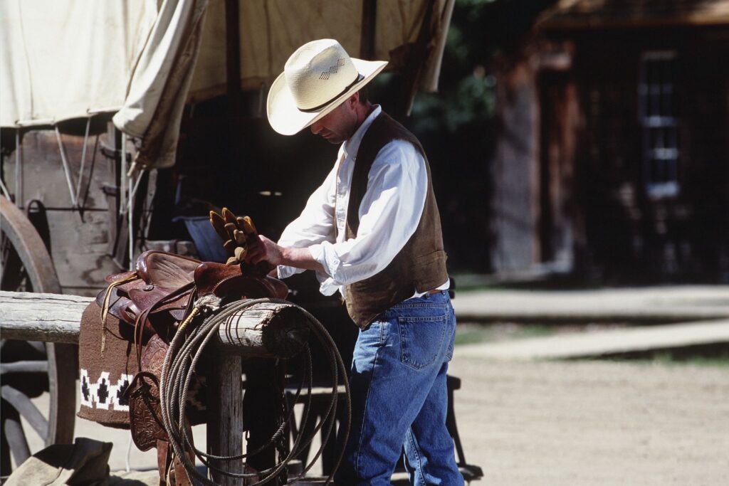 man wearing cowboy hat working on saddle