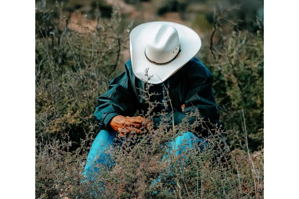 man sitting in brush wearing cowboy hat