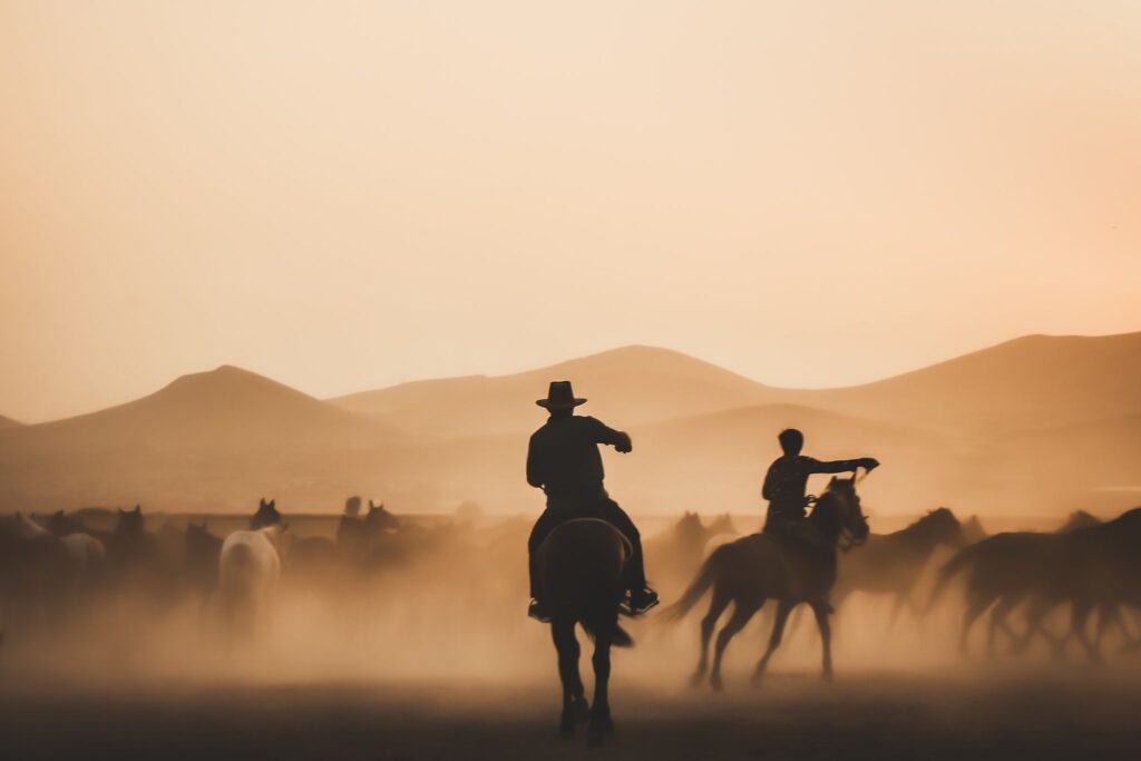 silhouettes of two people riding horses with mountain backdrop