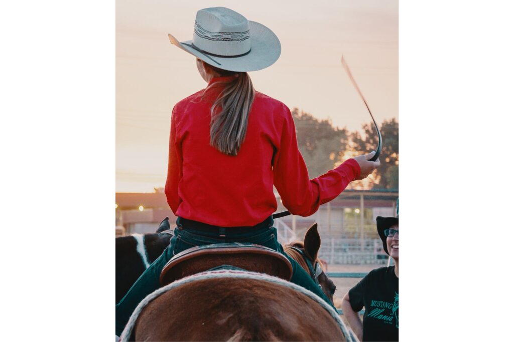 woman in red shirt wearing cowboy hat riding a horse