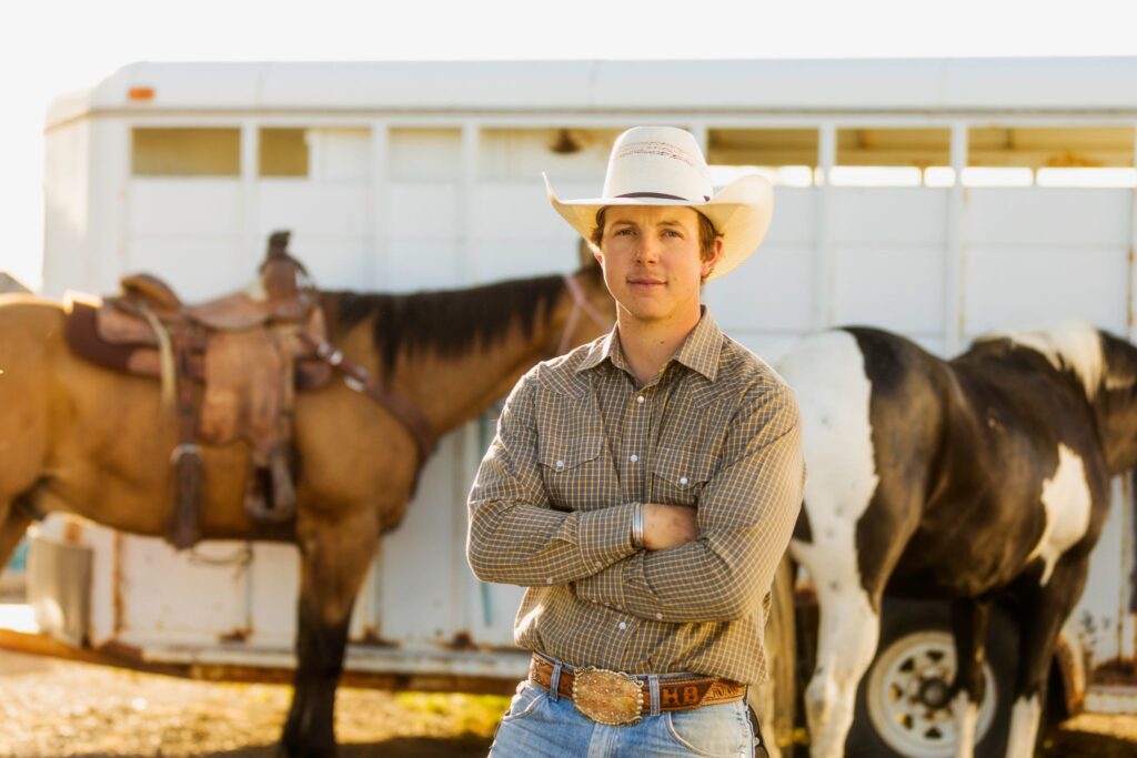 man wearing cowboy hat in front of horses and trailer