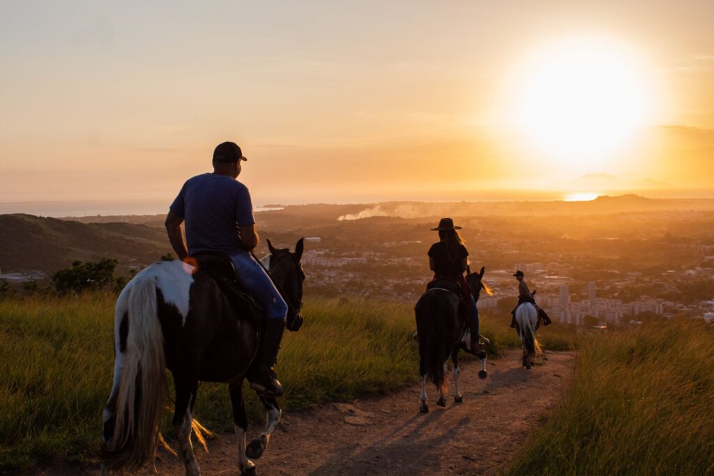 group of people trail riding horses at sunset