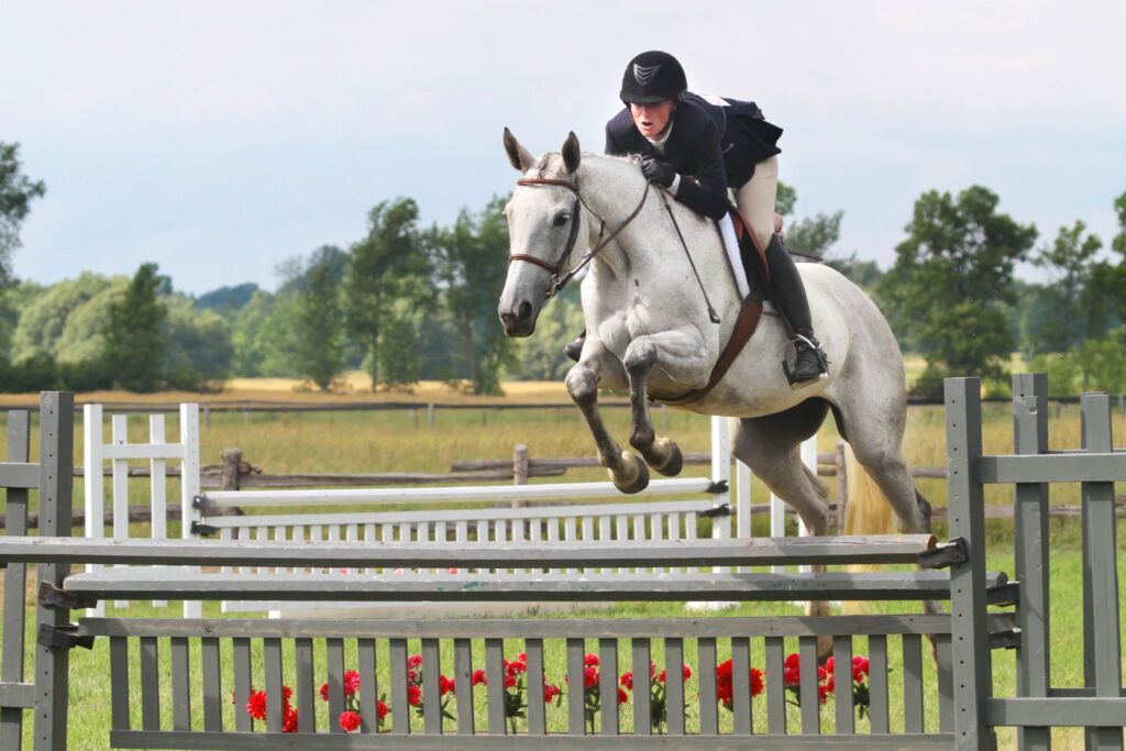 person riding gray horse over a fence
